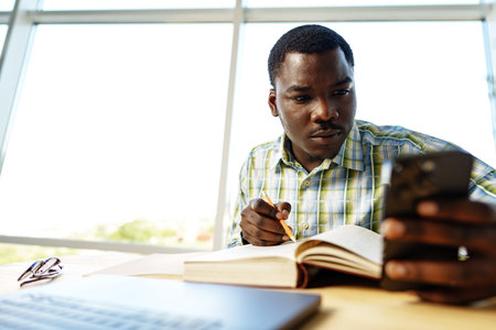 Young african man talking on the phone in office near windowの写真素材