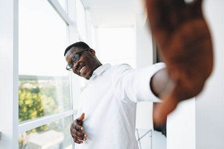 Young african man in white shirt and glasses posing near large windowの写真素材