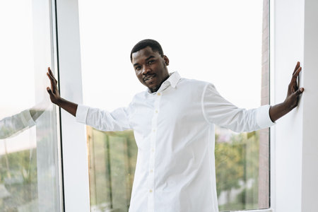 Young african man in white shirt and glasses posing near large window