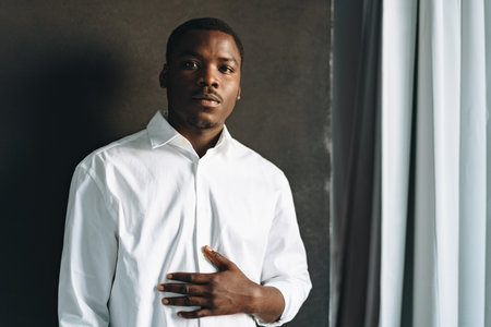 Close up portrait of young african man in white shirt against black wall in studioの写真素材