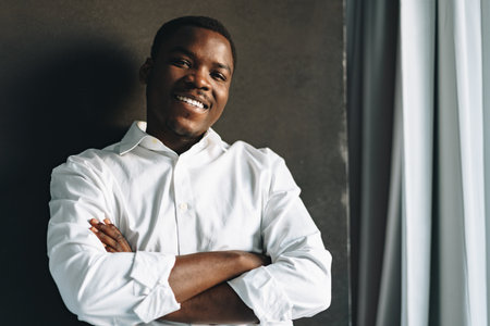Close up portrait of young african man in white shirt against black wall in studioの写真素材