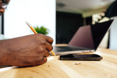 Close up photo of african businessman making notes while sitting at the table in officeの写真素材