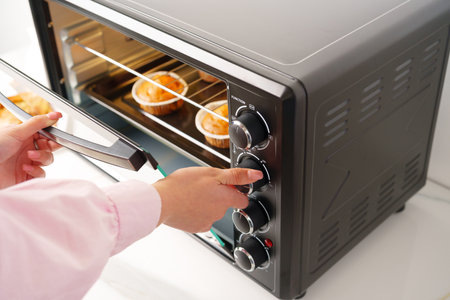 Womans hands taking buscuit cupcakes out of mini oven