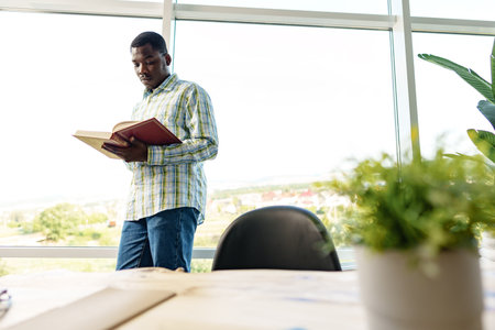 African man standing near the window in room and reading a bookの写真素材