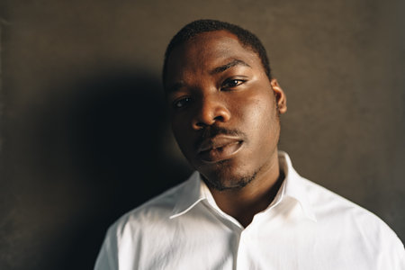 Close up portrait of young african man in white shirt against black wall in studioの写真素材