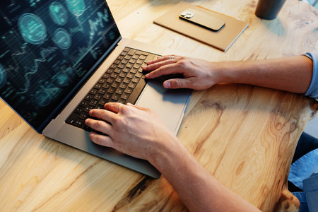 Mans hands using laptop on wooden desk