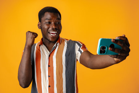 Young african man using smartphone againast yellow backgroundの写真素材