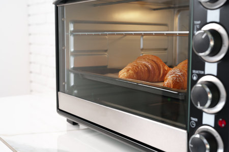 Modern mini electric oven with freshly baked croissants in kitchen