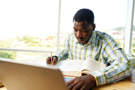 Serious concentrated african man studying or working with laptop indoorsの写真素材
