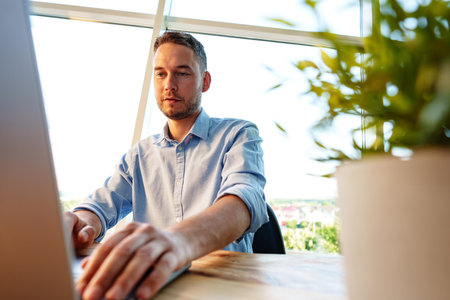 Portrait of young man sitting at his desk in the office and using computerの写真素材