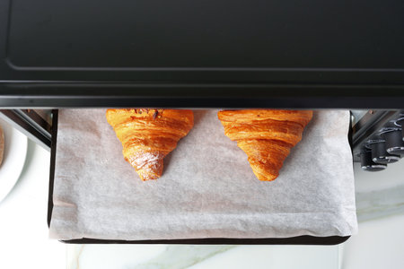 Modern electric oven with freshly baked croissants in kitchenの写真素材