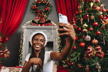 Young beautiful African woman using her phone at home decorated for Christmas seasonの写真素材