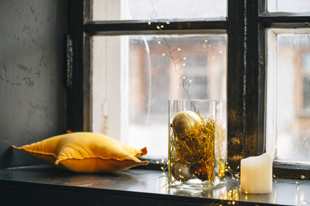 Black windowsill decorated for Christmas with golden baubles and candlesの写真素材