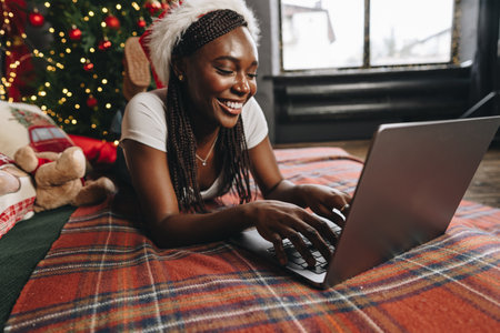 Young African woman on bed using laptop on Christmas eveの写真素材