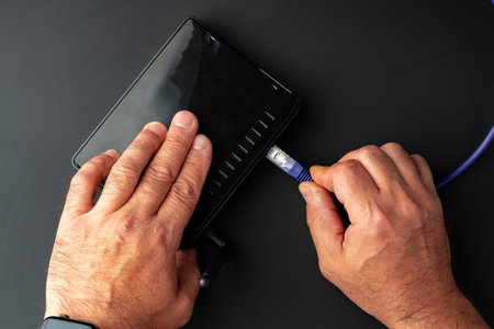 Mans hand plugging internet cable into wifi router