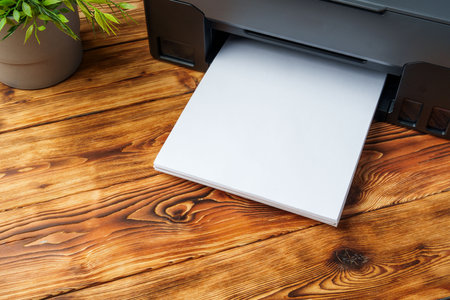 Modern laser printer with paper on wooden background