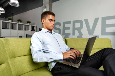 Handsome young businessman sitting in office lobby with a laptop