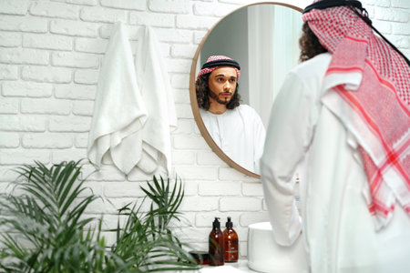Young Arab man getting ready and looking at the mirror in the bathroomの写真素材