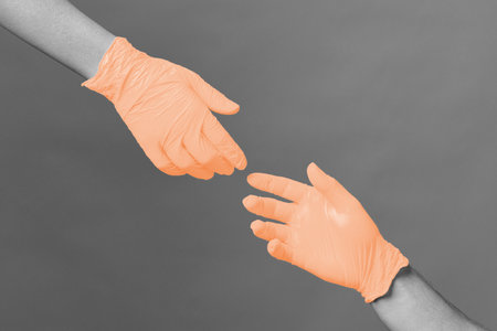 Hands in medical gloves stretch to each other against gray backgroundの写真素材