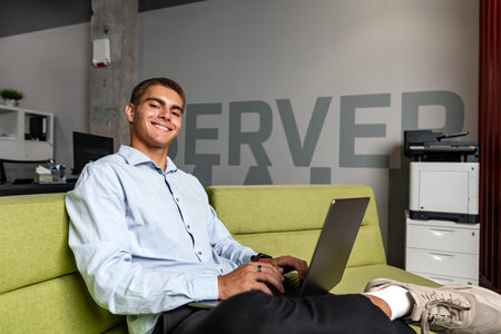 Handsome young businessman sitting in office lobby with a laptop