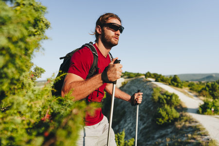 Young man hiker travels through the mountains with trekking poles for nordic walkingの写真素材