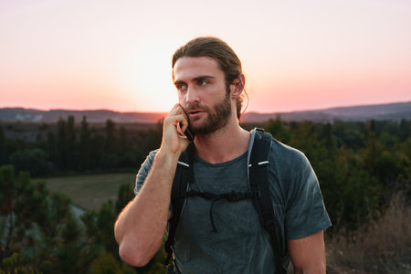 Male hiker with a backpack is talking on the phone in the countrysideの写真素材