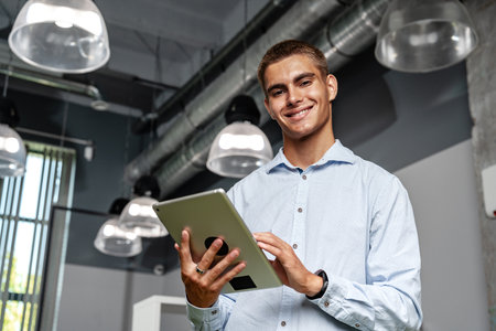Young handsome businessman using digital tablet while standing in the officeの写真素材