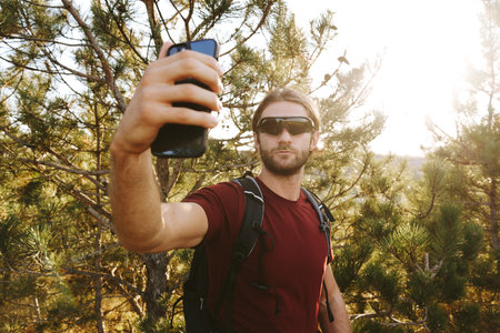 Hiker man in sunglasses using his mobile phone in the mountain woods