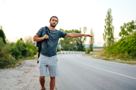 Young man hiker with backpack on hitchhiking near the roadの写真素材