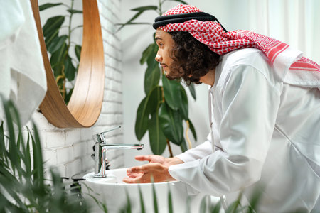 Young Arab man getting ready and looking at the mirror in the bathroomの写真素材