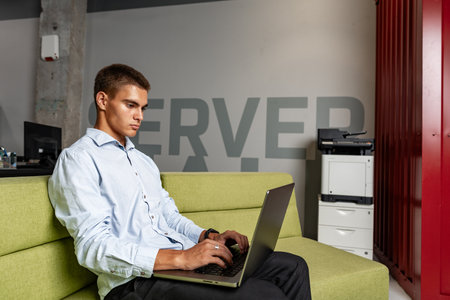 Handsome young businessman sitting in office lobby with a laptop