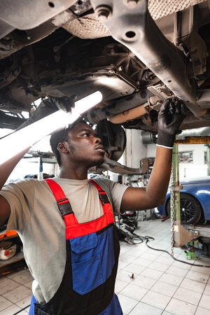 Young African mechanic in uniform working under the car in car service centerの写真素材