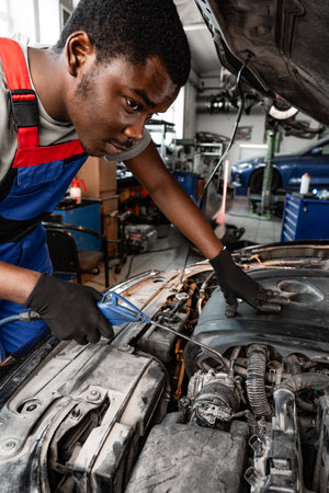 Young African auto mechanic checking car engine under the hood in auto service