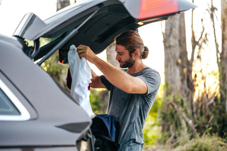 Young man changing clothes on the car trunk after hiking in the woodsの写真素材