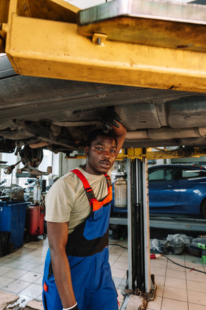 Young African mechanic in uniform working under the car in car service centerの写真素材