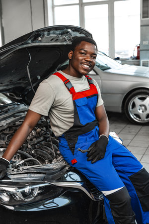Young African man working under the hood of car fixing engine in auto serviceの写真素材