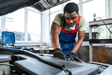 Young African man working under the hood of car fixing engine in auto serviceの写真素材