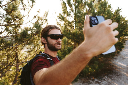 Hiker man in sunglasses using his mobile phone in the mountain woods
