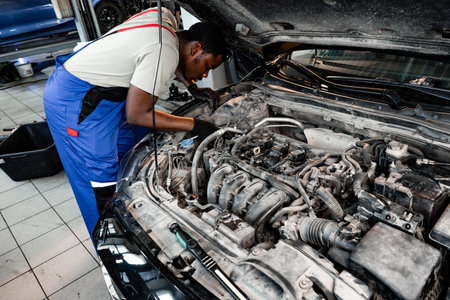 Young African auto mechanic checking car engine under the hood in auto service