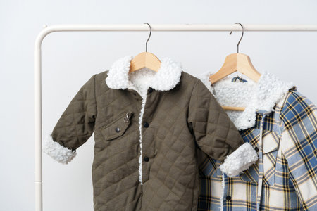 Two kids winter coats hanging on hangers against white wallの写真素材