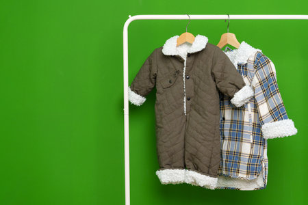Two kids winter coats hanging on hangers against green wall in studioの写真素材