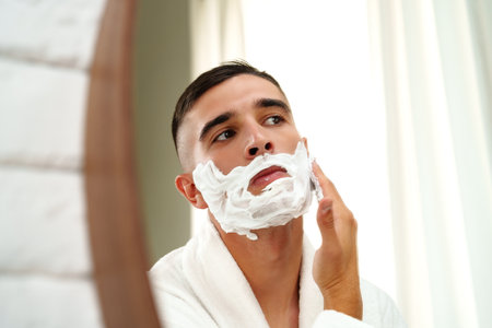 Reflection of a young man shaving in bathroom mirror close upの写真素材