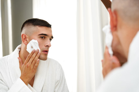 Reflection of a young man shaving in bathroom mirror close upの写真素材
