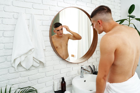 Young man looking in the mirror in the bathroom preparing for the dayの写真素材