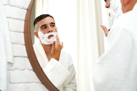 Reflection of a young man shaving in bathroom mirror close upの写真素材
