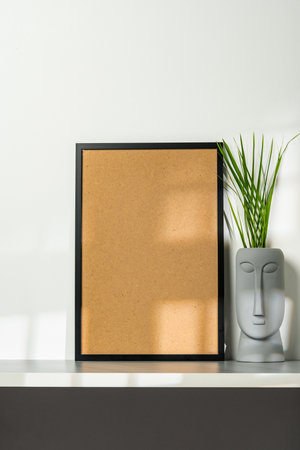 Black wooden frame and gray vase with plant leaves against white wallの写真素材