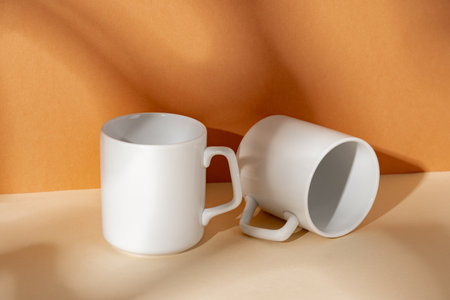 White ceramic mugs on peach background with shadowsの写真素材
