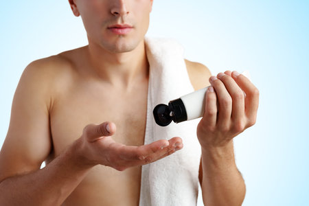 Young handsome man applies nourishing facial cream on white backgroundの写真素材