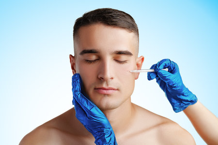 Handsome young man face and beautician hands with syringe making cosmetic injection in faceの写真素材