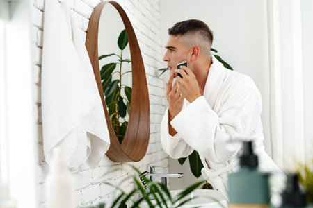 Reflection of a young man shaving in bathroom mirror close upの写真素材